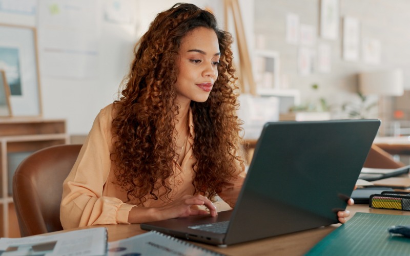 a young woman with curly hair uses a notebook computer to draft a business plan
