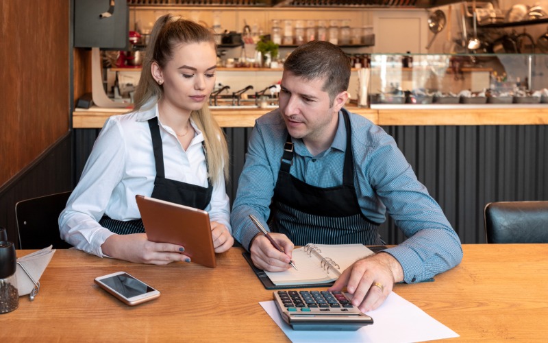 a man and woman use an adding machine to calculate growth costs for a small business