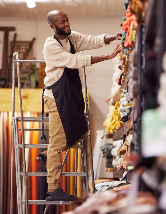 a man in southwest virginia stands on a ladder to inventory fabrics in a storage area