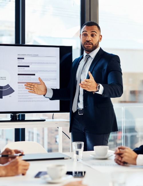 a charismatic man wearing a dark suit presents data in a business meeting